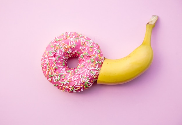 Donut doce fresco e banana em fundo rosa. Visão Abive