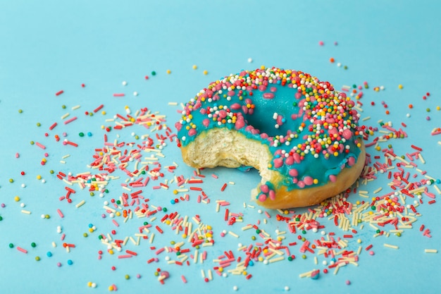 Donut (donut) de diferentes colores sobre un fondo azul con chispitas de azúcar festivas multicolores. Vacaciones y dulces, hornear para niños, concepto de azúcar