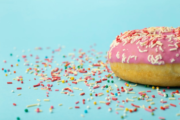 Donut (Donut) in verschiedenen Farben auf blauem Grund mit mehrfarbigen festlichen Zuckerstreuseln. Urlaub und Süßigkeiten, Backen für Kinder, Zuckerkonzept