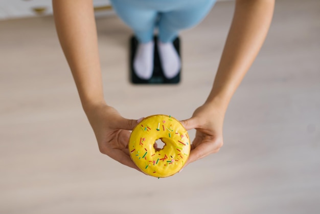 Foto donut dulce en las manos de una mujer de pie en la balanza