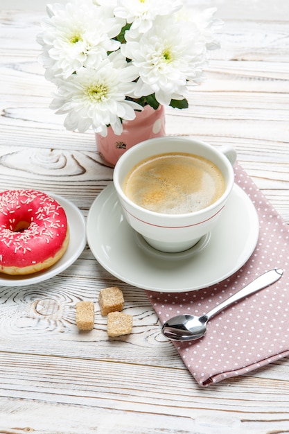 Donut e café, flores sobre fundo de madeira