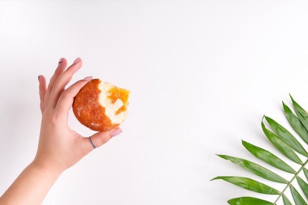 Donut fresco casero con mermelada de albaricoque en una mano de mujer en hoja de palma blanca y verde.