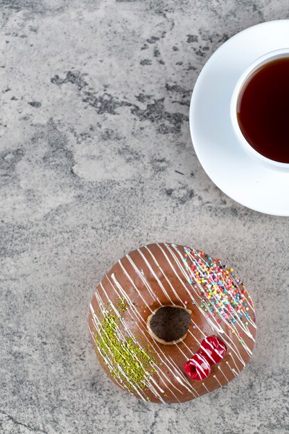 Donut glaseado chocolate delicioso y taza de té sobre fondo de piedra.