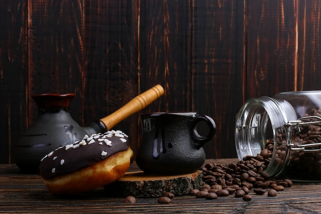 Donut con glaseado negro y chocolate en polvo y una auténtica taza de café fuerte. Una lata de granos de café y granos vertidos.