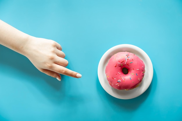 Donut con glaseado rosa y una mano femenina sobre un fondo azul.