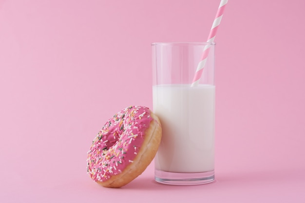 Donut glaseados con chispas y un vaso de leche sobre fondo rosa