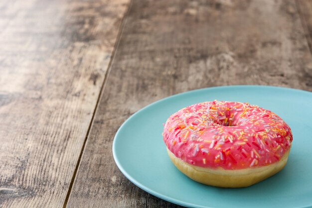 Donut helado rosa con chispitas de colores en el espacio de copia de mesa de madera