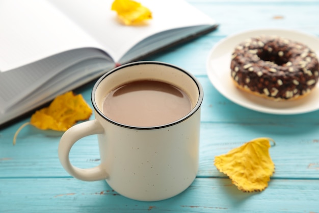 Donut, Kaffeetasse und Herbstlaub auf blauem Hintergrund, Ansicht von oben