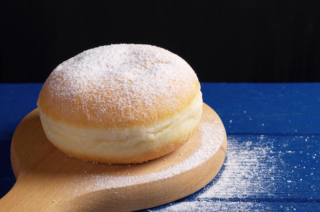 Donut con mermelada y azúcar en polvo en la tabla de cortar se encuentra en el primer plano de la mesa de madera azul