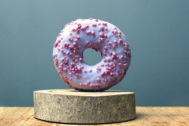 Donut mit lila Glasur auf einem Holzständer auf einem grauen Hintergrund. süßes Brötchen auf einem dekorativen Waldstand.