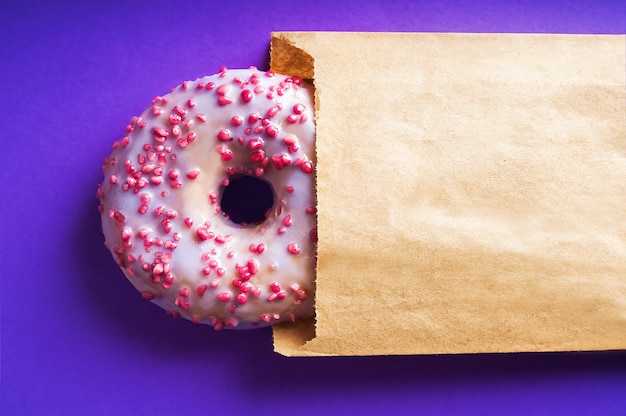 Donut mit lila und rosa Pulver Nahaufnahme auf blauem Tisch. Food Delivery-Konzept, Donut in Kraftpapier und Kopierraum.