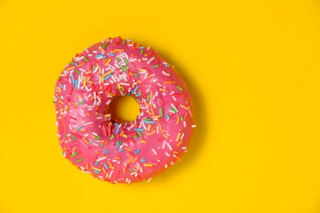 Donut mit rosa Zuckerguss und bunten Zuckerstreuseln auf gelbem Hintergrund