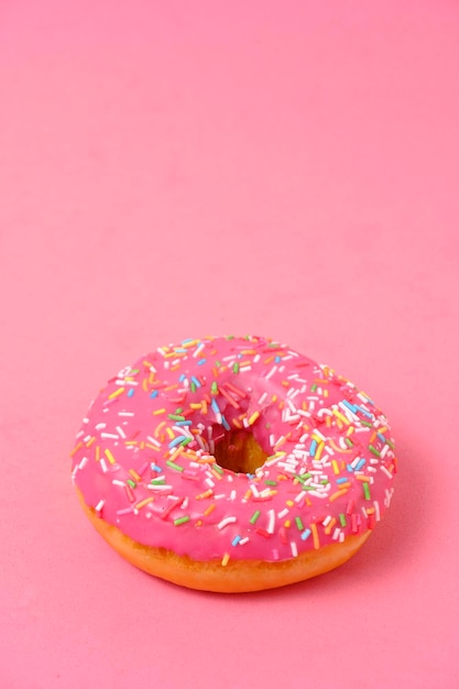 Donut mit rosa Zuckerguss und bunten Zuckerstreuseln auf rosa Hintergrund
