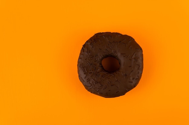 Donut mit Schokoladenglasur auf orangefarbenem Hintergrund