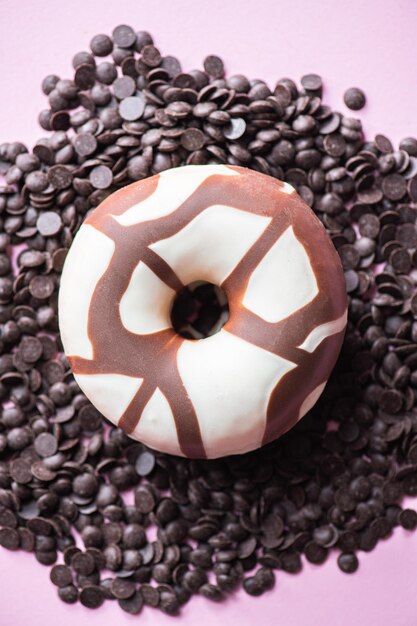 Donut mit Schokoladenglasur auf Schokoladenstückchen auf rosa Hintergrund Draufsicht