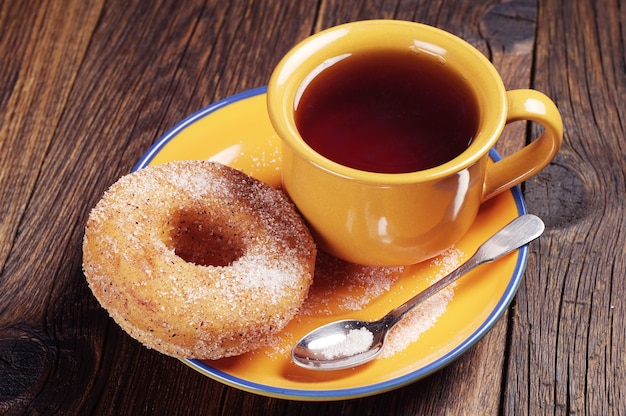Donut mit Zucker und heißem Tee auf Holztisch