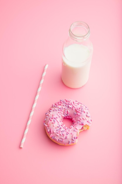 Donut rosa y botella de leche sobre fondo rosa