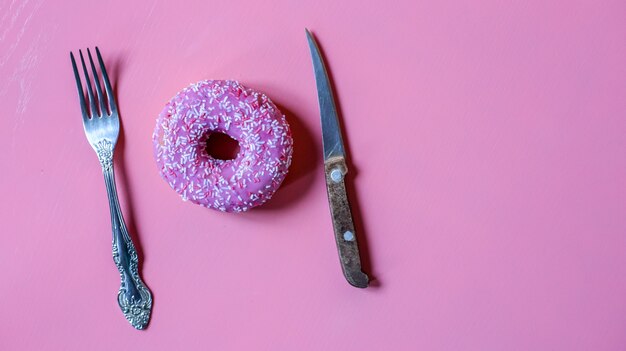 Donut rosa brillante en glaseado con cuchillo y tenedor