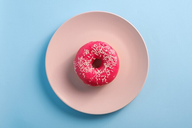 Donut rosa con chispitas en un plato rosa, postre dulce glaseado en azul mínimo