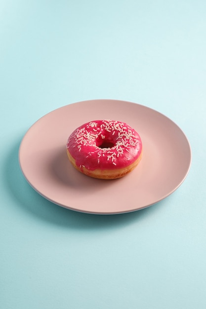 Donut rosa com granulado em prato rosa, sobremesa doce com cobertura em azul mínimo, vista angular