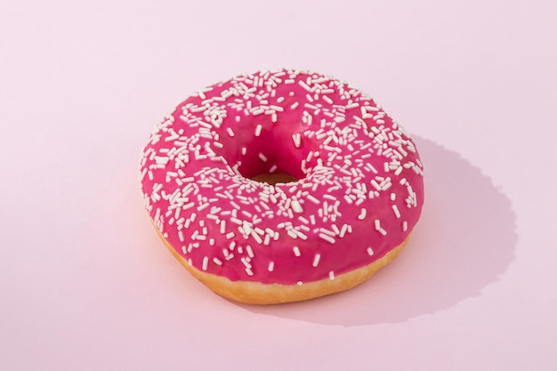 Donut rosa con glaseado sobre fondo rosa pastel.