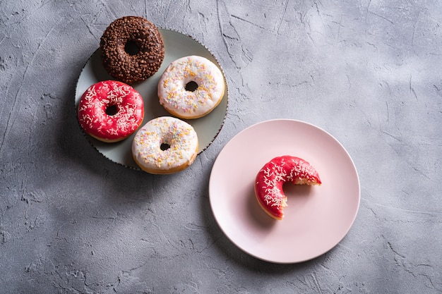 Donut rosa mordido con chispas en un plato rosa cerca de donas de chocolate y vainilla