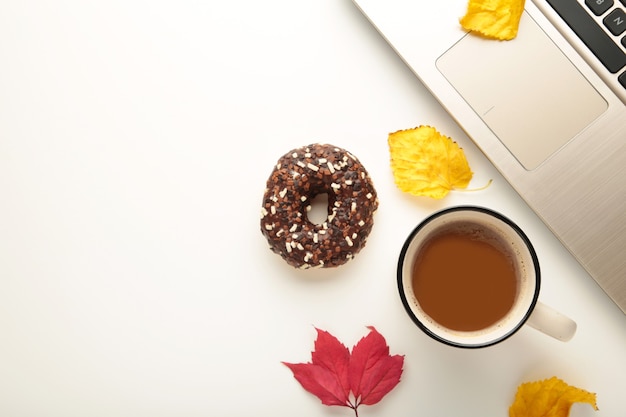 Donut, taza de café y hojas de otoño sobre fondo blanco, vista superior