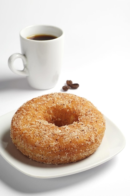 Donut y taza de café negro sobre fondo blanco.