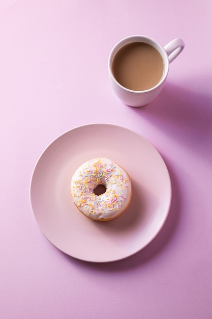 Donut de vainilla con chispas en un plato cerca de una taza de café