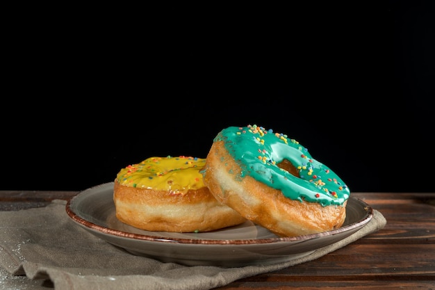 Donuts amarillos y verdes en un plato de diseño Expuesto en una bandeja de madera Fondo negro Vista lateral