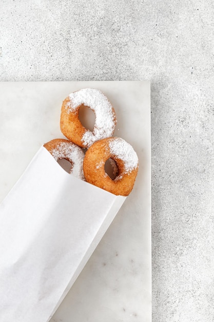 Donuts con azúcar en polvo en bolsa de papel artesanal para alimentos sobre fondo gris Comida para llevar