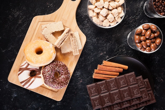 Donuts, cacahuetes en chocolate y granos de café sobre fondo de madera