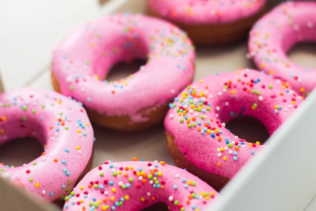 Foto donuts caseiros do círculo com glacê rosa e granulado do arco-íris na caixa branca no papel ofício.