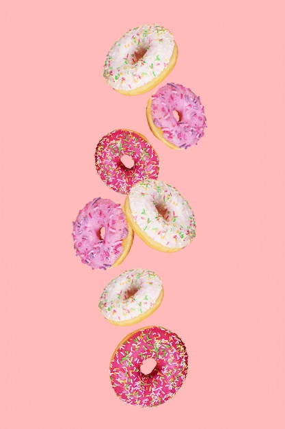 Donuts cayendo con esmalte de color sobre fondo rosa de moda. Levitando la comida.