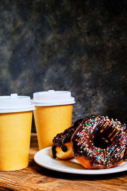 Donuts de chocolate y café para llevar sobre un fondo oscuro.