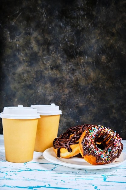 Donuts de chocolate y café para llevar sobre un fondo oscuro.