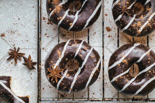 Donuts de chocolate y vainilla con canela, cacao y anís estrellado sobre fondo de baldosas blancas