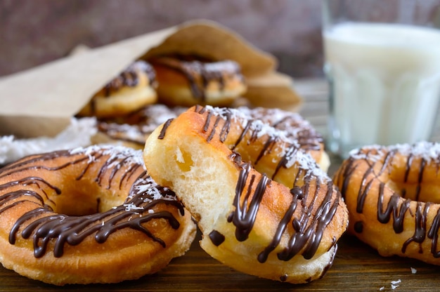 Donuts clásicos caseros con copos de chocolate y coco y un vaso de leche sobre un fondo de madera oscura. De cerca.