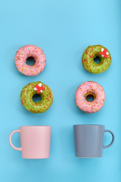 Donuts coloridos com cobertura e xícaras de café na superfície azul pastel