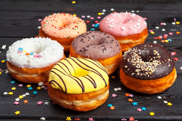 Donuts coloridos decorados con confeti rocía sobre fondo de madera oscura