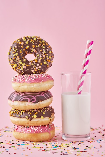 Donuts coloridos esmaltes com granulado e copo de leite em fundo rosa