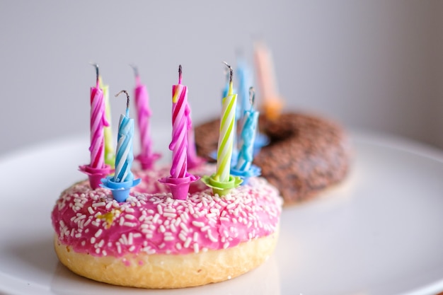 Donuts coloridos con glaseado rosa y chocolate con velas para fiesta de cumpleaños