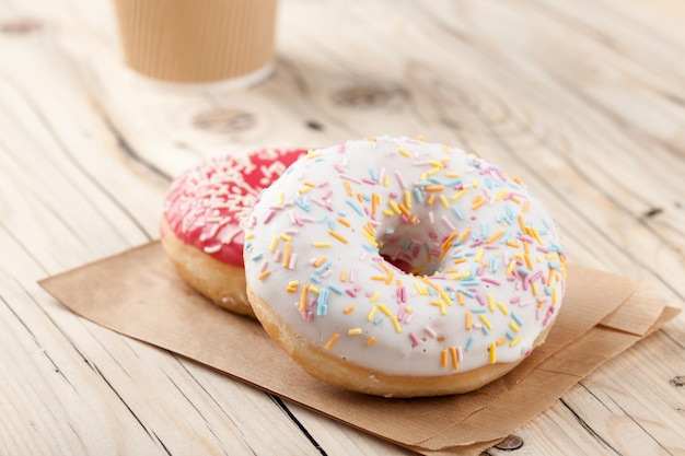 Donuts coloridos y vaso de papel sobre la mesa de madera, cerrar