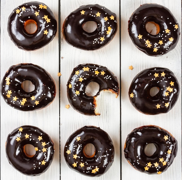 Donuts com cobertura de espelho de chocolate e granulado sobre fundo branco de madeira Vista superior