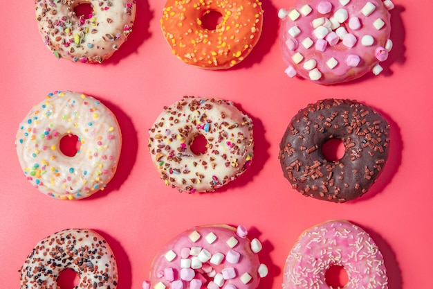 Donuts com glacê em fundo rosa pastel rosquinhas doces vista superior sortidas com vários gl de chocolate