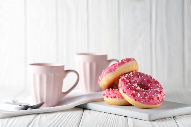 Donuts com pó de caramelo colorido e glacê rosa em um fundo branco de madeira