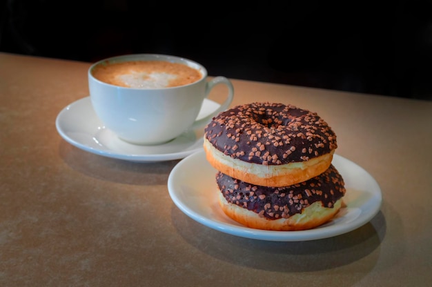 Donuts cubiertos de chocolate y taza blanca de capuchino