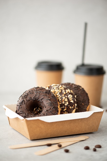 Donuts de chocolate com cobertura em uma caixa artesanal e café preto em xícaras em uma mesa branca