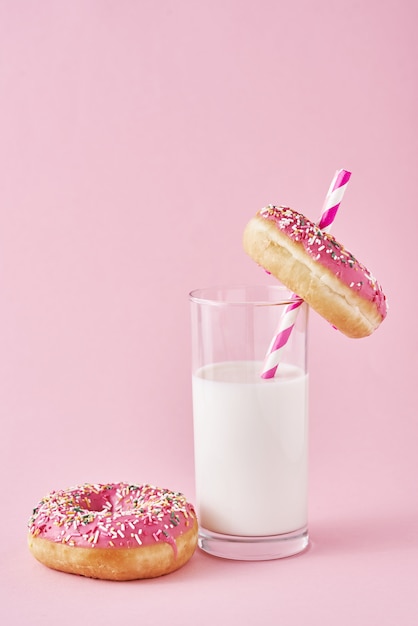 Donuts decorados com glacê e polvilhe e copo de leite na rosa