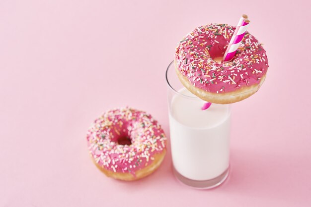 Donuts decorados com glacê e polvilhe e copo de leite no fundo rosa